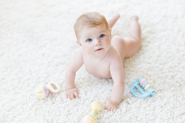 Renkli pastel antika çıngıraklı oyuncakla oynayan şirin bir bebek. Yeni doğmuş bir çocuk, küçük bir kız kameraya bakıyor ve emekliyor. Aile, yeni hayat, çocukluk, başlangıç konsepti. Bebek yakalama.