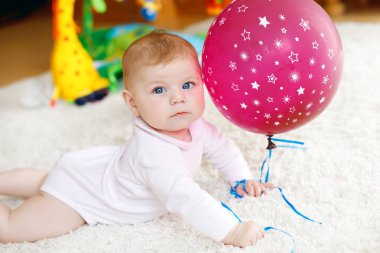 Kırmızı hava balonuyla oynayan şirin bir bebek. Yeni doğmuş çocuk, küçük kız eğleniyor, kavrıyor ve sürünüyor. Aile, yeni hayat, çocukluk, başlangıç konsepti. Bebek yakalama.