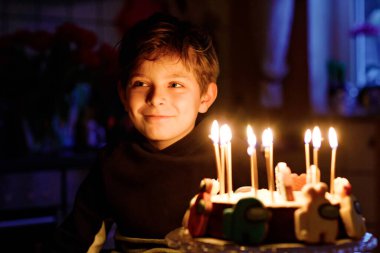 Sevimli, mutlu, küçük sarışın çocuk doğum gününü kutluyor. Çocuk ev yapımı kek üzerine mum üflüyor, kapalı alanda. Okul çocukları için doğum günü partisi, aile kutlaması