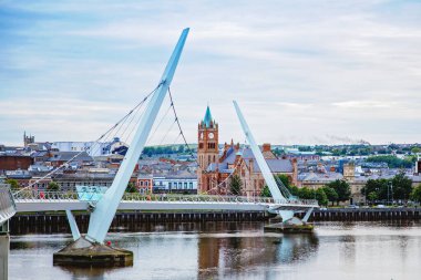 Derry, İrlanda. Kuzey İrlanda 'da, Derry Londonderry' de, Kültür Şehri 'nde şehir merkezinde aydınlatılmış bir barış köprüsü. Gece bulutlu gökyüzü, alacakaranlıkta nehirde yansıyor.