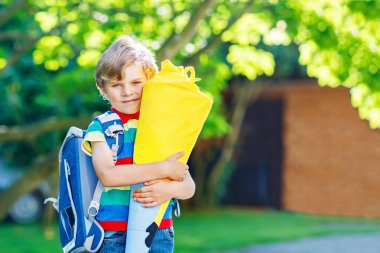 Renkli tişörtlü, sırt çantalı mutlu bir çocuk ya da çantalı ve Schultuete adındaki geleneksel Alman okul çantalı. Okuldaki ilk gününde hediye almış. Sıcak ve güneşli bir günde çocuk dışarıda..