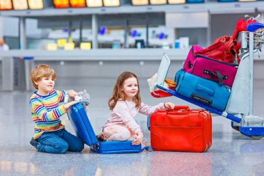 İki küçük çocuk, havaalanında bavulları olan kız ve erkek, içeride ve aile tatiline çıkmayı bekliyorlar. Mutlu çocuklar, ikizler, erkek kardeşler ve kız kardeşler...