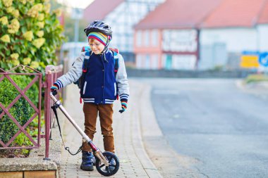 Kasklı aktif okul çocuğu şehirde scooterıyla geziyor. Renkli elbiseli mutlu çocuk okula giderken bisiklete biniyor. Çocuklar için güvenli okul yolu.