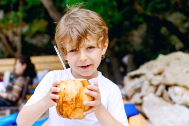 Okyanus sahilinde hindistan cevizi suyu içen komik anaokulu çocuğu. Çocuklar tropik adalarda aile tatillerinde oynuyorlar. Yaz, mutluluk, çocukluk konsepti. Seçici odak.