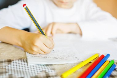 Ödev yapan ve hikaye kompozisyonu yazan bir çocuğun yakın çekimi. İlkokul ya da ilkokul. Ellerin ve renkli kalemlerin yakınlaşması. Coronavirüs zamanında evde eğitim, okullar kapalı..