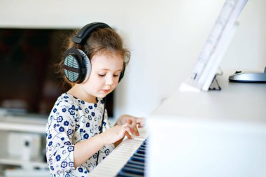 Oturma odasında ya da müzik okulunda kulaklıkla piyano çalan güzel bir kız çocuğu. Anaokulu çocuğu müzik aleti çalmayı öğrenirken eğleniyor. Eğitim, beceri kavramı