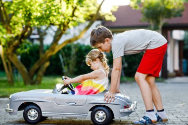 İki mutlu çocuk açık havada, yaz bahçesinde eski oyuncak arabalarıyla oynuyorlar. Çocuk itip kakıyor ve içinde küçük bir kız, içinde de tatlı bir kız kardeşi olan arabayı sürüyor. Gülen ve gülümseyen çocuklar. Güzel aile.
