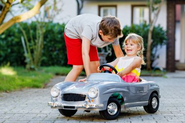 İki mutlu çocuk açık havada, yaz bahçesinde eski oyuncak arabalarıyla oynuyorlar. Çocuk itip kakıyor ve içinde küçük bir kız, içinde de tatlı bir kız kardeşi olan arabayı sürüyor. Gülen ve gülümseyen çocuklar. Güzel aile.
