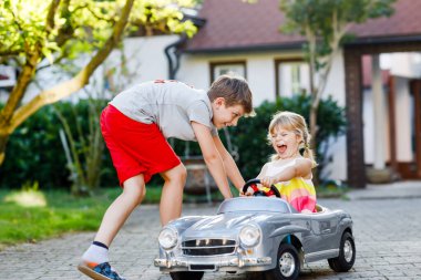 İki mutlu çocuk açık havada, yaz bahçesinde eski oyuncak arabalarıyla oynuyorlar. Çocuk itip kakıyor ve içinde küçük bir kız, içinde de tatlı bir kız kardeşi olan arabayı sürüyor. Gülen ve gülümseyen çocuklar. Güzel aile.