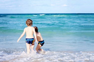 Okyanus sahilinde koşan iki mutlu çocuk. Komik şirin çocuklar, kardeşler, ikizler ve en iyi arkadaşlar tatile çıkıyor ve yaz gününün tadını çıkarıyor. Dalgalara atlarken eğleniyorum..
