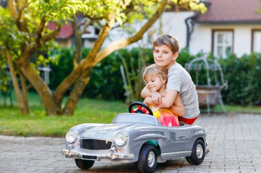 İki mutlu çocuk açık havada, yaz bahçesinde eski oyuncak arabalarıyla oynuyorlar. Çocuk itip kakıyor ve içinde küçük bir kız, içinde de tatlı bir kız kardeşi olan arabayı sürüyor. Gülen ve gülümseyen çocuklar. Güzel aile.
