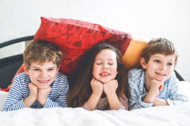 Pijamalı üç mutlu çocuk pijama partisini kutluyor. Anaokulu ve okul çocukları ve kız birlikte eğleniyorlar.