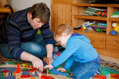Baba ve küçük çocuk içeride ahşap demiryolu ile oynuyorlar. Mutlu aile, adam ve tatlı çocuk trenleri taşıyor..