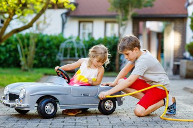 İki mutlu çocuk açık havada, yaz bahçesinde eski oyuncak arabalarıyla oynuyorlar. Delikanlı çocuk, içinde küçük bir kız çocuğu, içinde de tatlı bir kız kardeşi olan bir yakıt deposu. Çocuk bahçe hortumu kullanıyor ve benzin dolduruyor, kardeşim.