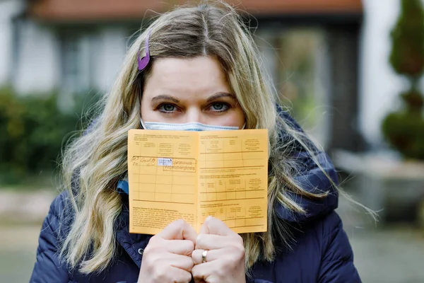 Woman with medical mask holding German inernational certificate of the vaccination. Adult showing the information about her vaccine against covid 19 corona virus. — Stock Photo, Image