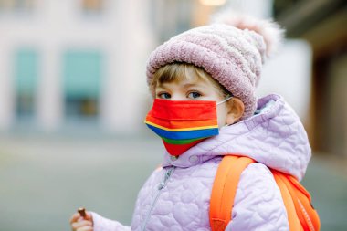 Anaokuluna, çocuk parkına ya da kreşe giderken maske takan küçük bir çocuk. Soğuk bir günde sırt çantalı bir çocuk ve sıcak giysiler. Corona salgını sırasında tecrit ve karantina süresi