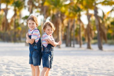 İki küçük çocuk tropikal plajda eğleniyor, mutlu arkadaşlar oynuyor, arkadaşlık kavramı. Kardeşler, ailedeki ikizler arka planda avuç içleri olan tipler. İspanya 'da aile tatilleri.