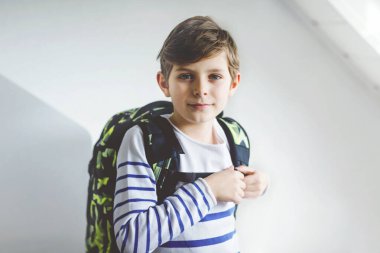 Okul çantalı güzel çocuk sabahın erken saatlerinde odada duruyor. Okula ve derslere giden mutlu sağlıklı çocuk. Eğitim kavramı