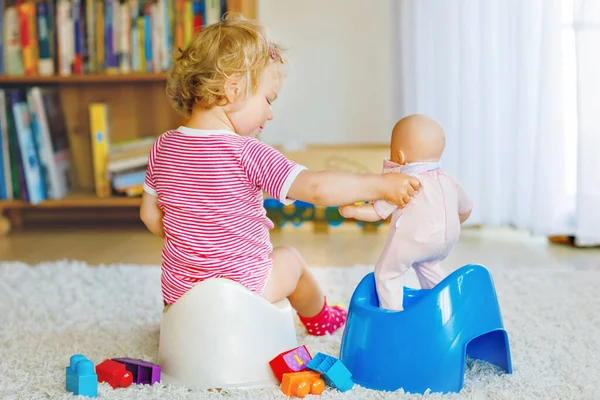 Closeup of cute little 12 months old toddler baby girl child sitting on potty. Kid playing with doll toy. Toilet training concept. Baby learning, development steps