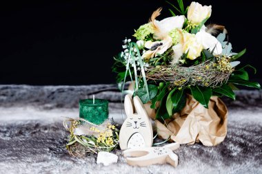 Decoration for Easter holiday or spring with soft flower arrangement, green candle and wooden bunnies and eggs.