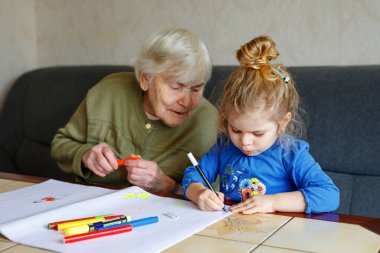 Güzel bir kız ve büyükanne evde keçeli kalemle resim çiziyorlar. Tatlı çocuk ve son sınıf öğrencisi birlikte eğleniyorlar. Mutlu aile içeride.