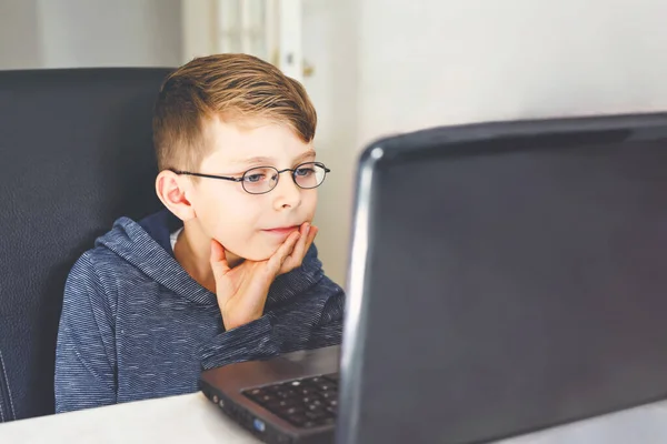 Garoto com óculos aprendendo em casa no laptop para a escola. Criança adorável fazendo lição de casa e usando notebook e gadgets modernos. Conceito de escola doméstica. — Fotografia de Stock