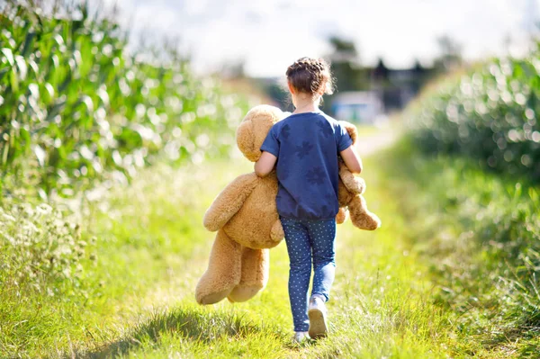 Menina bonito brincando com dois peluches de brinquedo empurrar. Criança segurando enorme urso e pequeno urso e andando na paisagem da natureza — Fotografia de Stock