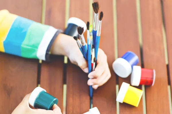 Närbild av händer barn som håller akvareller och borstar. Barn och elev är tillbaka i skolan. Utbildning, skola, lärande koncept. Skolutrustning, förskoleutrustning — Stockfoto