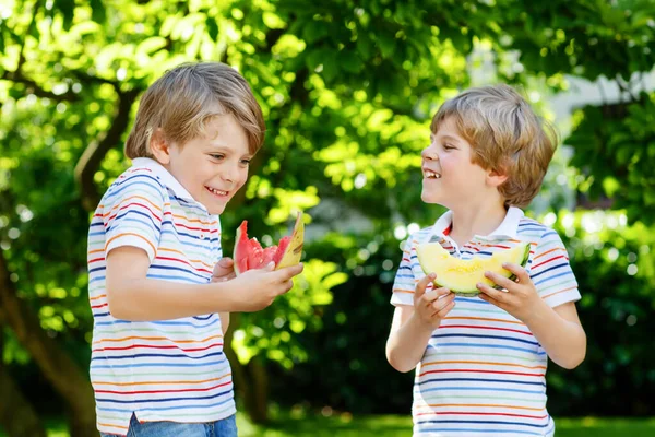 Två små förskolekillar som äter röd och gul vattenmelon i sommarträdgården. Roliga glada barn ler, med hälsosam frukt mellanmål på solig dag. Syskon, tvillingar och bästa vänner utomhus. — Stockfoto