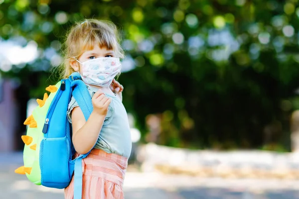 Pieni surullinen lapsi tyttö lääketieteen naamio vastaan korona virus covid matkalla lastentarhaan tai leikkikouluun. Onneton järkyttynyt lapsi häiritsevällä naamiolla. Lapset, joilla on mielenterveysongelmia johtuen sepelvaltimoviruksen lukitus — kuvapankkivalokuva