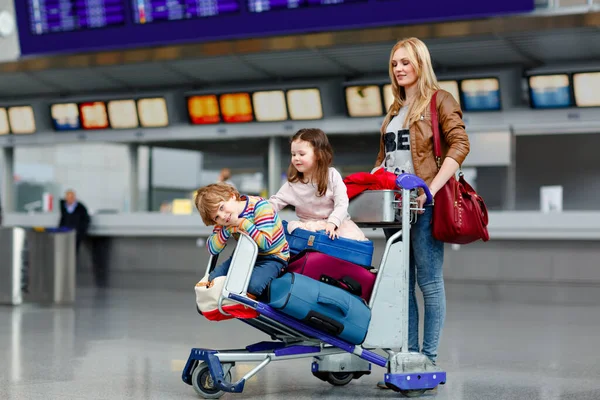 Due bambini piccoli, maschio e femmina, fratelli e madre all'aeroporto. Bambini, famiglia che viaggia, va in vacanza in aereo e aspetta sul carrello con valigie spingendo da donna al terminal per il volo. — Foto Stock