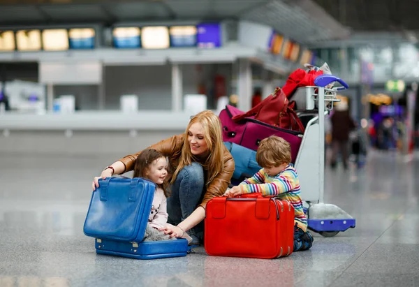 Zwei müde kleine Kinder, Junge und Mädchen, Geschwister und Mutter am Flughafen. Kinder, Familien, die mit dem Flugzeug in den Urlaub fliegen und mit dem Gepäckwagen mit Koffern am Terminal auf den Flug warten. — Stockfoto