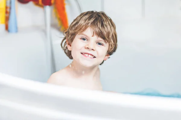 Cute little child playing with water by taking bath in bathtub at home. Adorable kid boy having fun, washing hair and splashing with soap — Stock Photo, Image