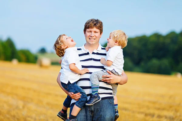 Father holding two children on arms on wheat field in summer — Stock Photo, Image