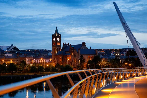 Derry, Ireland. Illuminated Peace bridge in Derry Londonderry, City of Culture, in Northern Ireland with city center at the background. Night cloudy sky with reflection in the river at the dusk — Stock Photo, Image