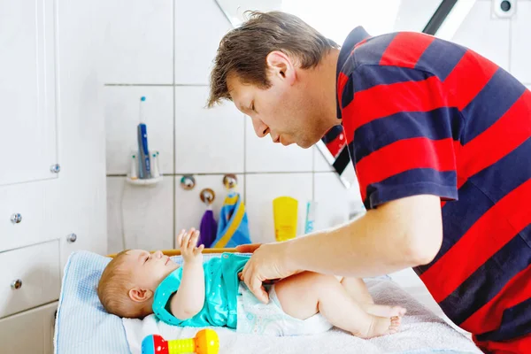 Loving father changing diaper of his newborn baby daughter. Little child, girl on changing table in bathroom with rattle toys. Happy dad. Family in love playing together — Stockfoto