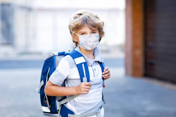 Happy little kid boy with medical mask and satchel walk to school. Schoolkid on way to school after lockdown. Healthy child outdoors. Back to school. Closed school due to corona virus covid pandemic — Foto Stock