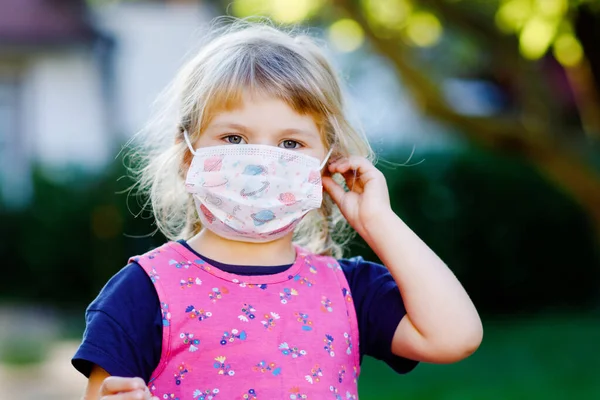 Pequena menina criança triste com máscara médica contra o vírus da corona covid a caminho do berçário ou playschool. Criança chateada infeliz com máscara perturbadora. Crianças com problemas mentais devido ao bloqueio do coronavírus — Fotografia de Stock