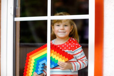 Pencere kenarındaki sevimli küçük kız pandemik koronavirüs karantinası sırasında renkli plastik bloklarla gökkuşağı yaratıyor. Dünyanın dört bir yanında çocuklar gökkuşağını işaret olarak yapıyor ve boyuyor.