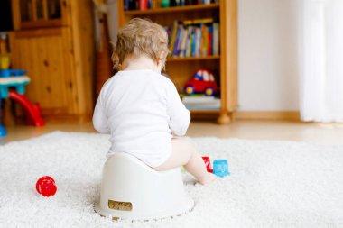 Lazımlığın üzerinde oturan küçük, tatlı, yaşlı, küçük kız bebek. Çocuk eğitim oyuncağı ve tuvalet eğitimi konseptiyle oynuyor. Bebek öğrenme, gelişme adımları. Yüzü yok, tanınmayan biri..