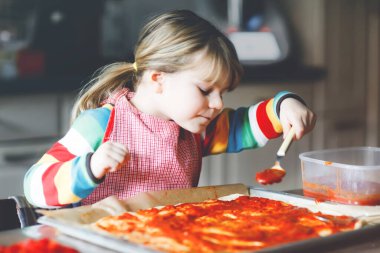 Sevimli küçük kız evde İtalyan pizzası yapıyor. Ev mutfağında, evde eğlenen sevimli mutlu çocuk. Çocuk, anaokulu öğrencisi sağlıklı yemek hazırlıyor ve yardım ediyor.