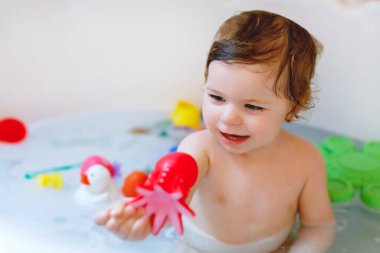 Küvette köpüklü banyo yapan sevimli, sevimli bir kız. Bebek banyo lastiğiyle oynuyor..