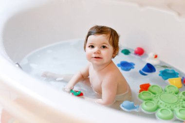 Küvette köpüklü banyo yapan sevimli, sevimli bir kız. Bebek banyo lastiğiyle oynuyor..