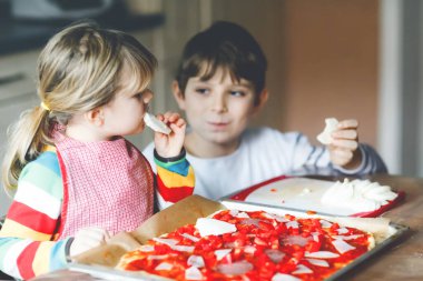 İki kardeş, evde İtalyan pizzası yapan küçük çocuklar. Şirin kız ve okul çocuğu ev mutfağında, evde eğleniyorlar. Erkek ve kız kardeş, aile yemeği hazırlıyor.