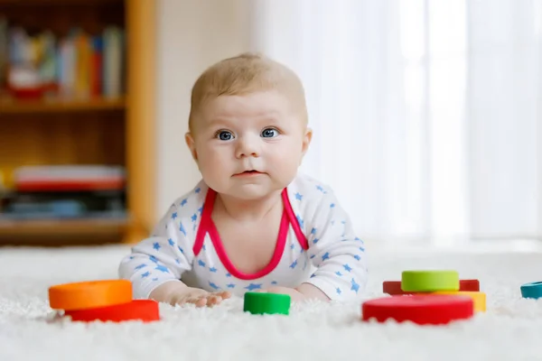 Χαριτωμένο αξιολάτρευτο νεογέννητο μωρό παίζει με πολύχρωμο ξύλινο κουδουνίστρα μπάλα παιχνίδι σε λευκό φόντο. Νεογέννητο παιδί, μικρό κορίτσι που κοιτάζει την κάμερα. Οικογένεια, νέα ζωή, παιδική ηλικία, έννοια έναρξης. — Φωτογραφία Αρχείου
