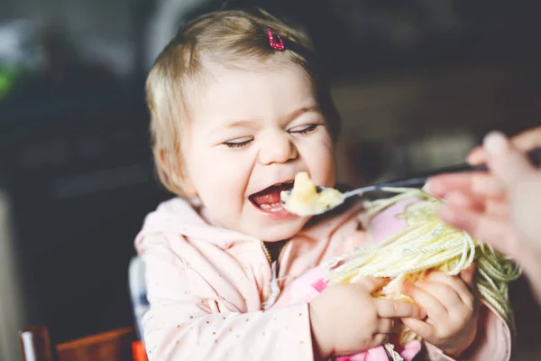 スプーンマッシュ野菜とピューレから食べる愛らしい赤ちゃんの女の子。食べ物、子供、食事、人の概念-かわいい幼児、椅子に座って家で食べるスプーンを持つ娘. — ストック写真