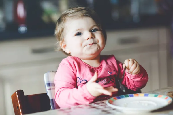 Menina bebê feliz comendo croissant fresco para o café da manhã ou almoço. Alimentação saudável para crianças. Criança em pijama colorido sentado na cozinha doméstica depois de dormir de manhã — Fotografia de Stock