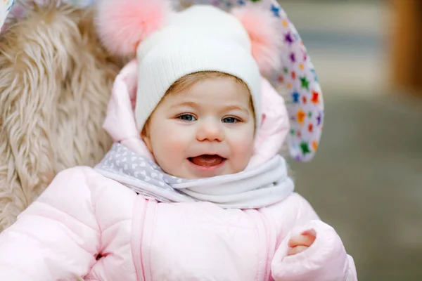 Söt liten vacker liten flicka sitter i barnvagn eller barnvagn på kall höst, vinter eller vår dag. Glad leende barn i varma kläder, mode snygg baby jacka och hatt. Snö faller ner — Stockfoto