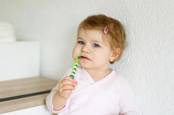Little baby girl holding toothbrush and brushing first teeth. Toddler learning to clean milk tooth. Prevention, hygiene and healthcare concept. Happy child in bathroom — Stock Photo, Image