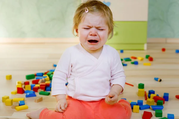 Zaklatott síró kislány oktatási játékokkal. Szomorú fáradt vagy éhes egyedül egészséges gyermek ül közelében színes különböző fatömbök otthon vagy óvoda. Eltűnt anya a bölcsiben. — Stock Fotó